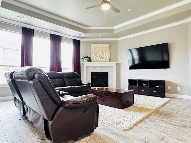 living room with a tray ceiling, visible vents, a ceiling fan, and light wood finished floors