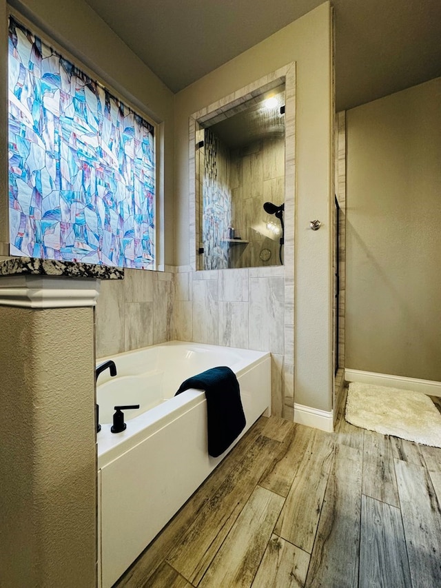 bathroom with a bath, tiled shower, baseboards, and wood finished floors