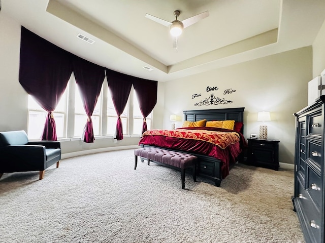 carpeted bedroom with visible vents, baseboards, a tray ceiling, and a ceiling fan