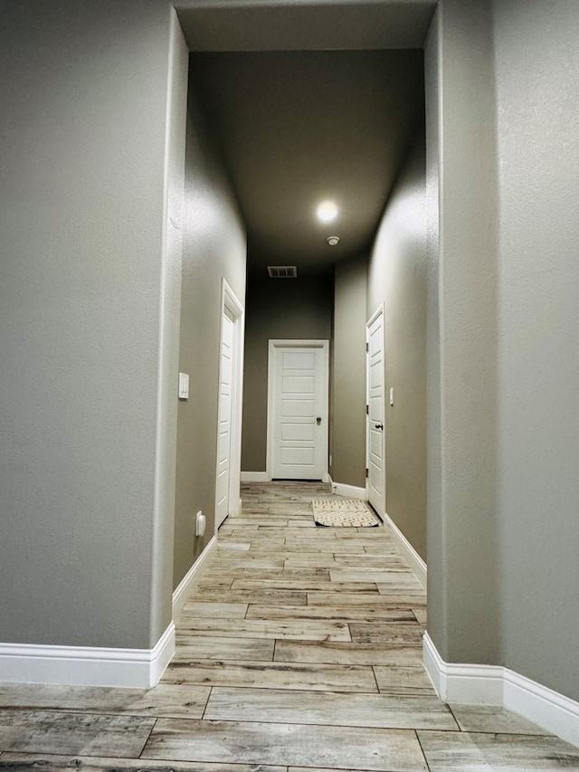 hall with visible vents, baseboards, and light wood-style floors