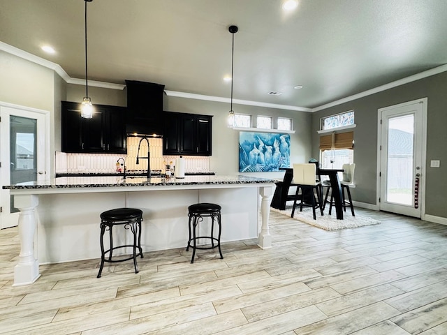 kitchen featuring tasteful backsplash, a breakfast bar, light wood-type flooring, dark stone counters, and dark cabinetry