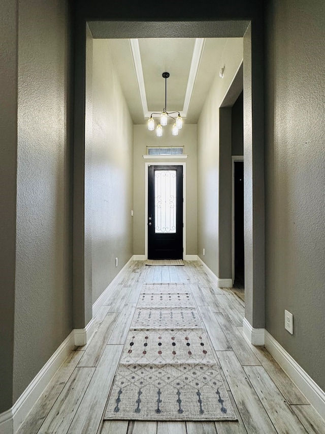 entryway with wood finish floors, a raised ceiling, an inviting chandelier, and a textured wall