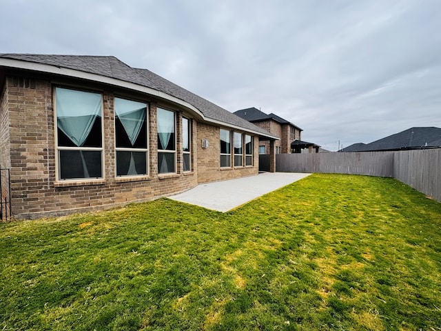 back of house featuring brick siding, a yard, a patio, and a fenced backyard