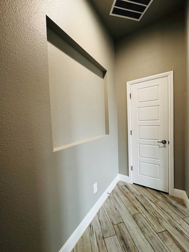 corridor featuring visible vents, baseboards, and wood finished floors