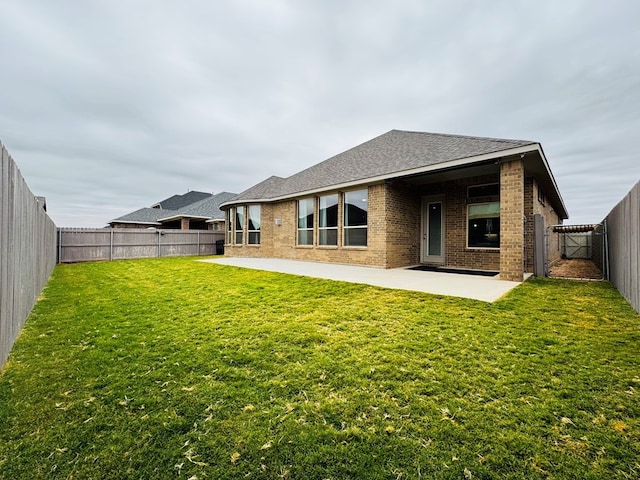 back of property featuring brick siding, roof with shingles, a fenced backyard, a yard, and a patio area