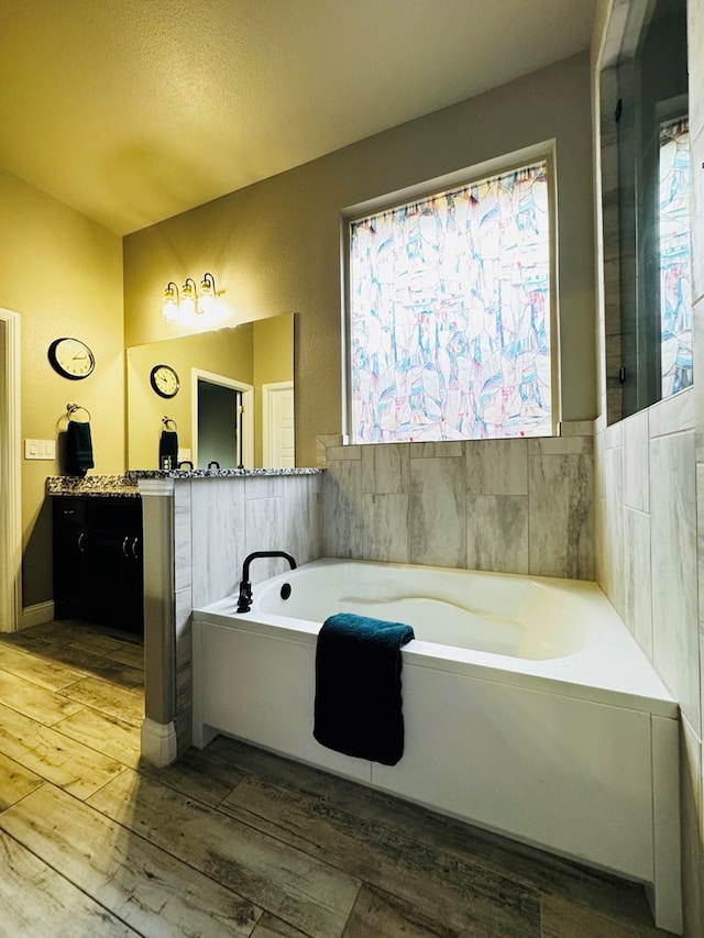 full bath with wood finished floors, a healthy amount of sunlight, a bath, and vanity