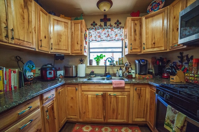 kitchen featuring black gas range, dark stone countertops, and sink