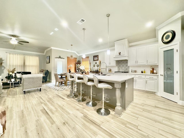 kitchen with ceiling fan, light wood-type flooring, an island with sink, decorative light fixtures, and white cabinetry