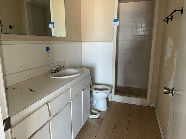 bathroom featuring a tile shower, hardwood / wood-style floors, vanity, and toilet