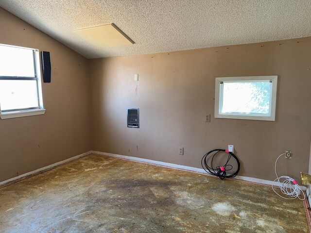 spare room with concrete flooring, a textured ceiling, vaulted ceiling, and a healthy amount of sunlight