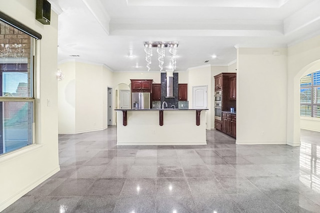 kitchen featuring backsplash, wall chimney range hood, appliances with stainless steel finishes, an island with sink, and a breakfast bar area