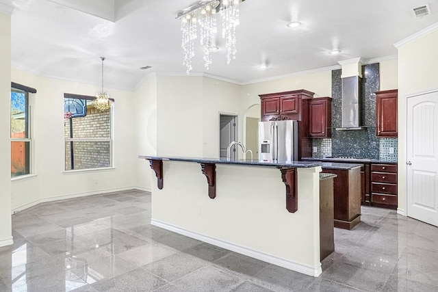 kitchen featuring tasteful backsplash, wall chimney range hood, a breakfast bar, high quality fridge, and a kitchen island with sink