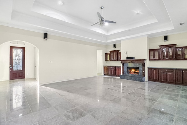 living room featuring ceiling fan, a high end fireplace, and a tray ceiling