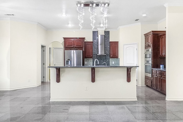 kitchen featuring appliances with stainless steel finishes, a center island with sink, wall chimney exhaust hood, and a breakfast bar area