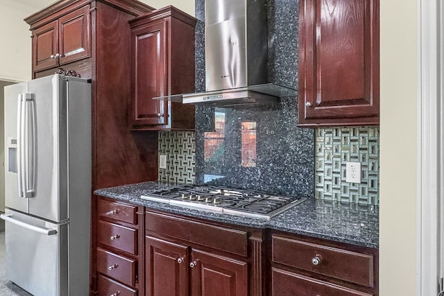 kitchen with stainless steel appliances, wall chimney exhaust hood, dark stone countertops, and tasteful backsplash