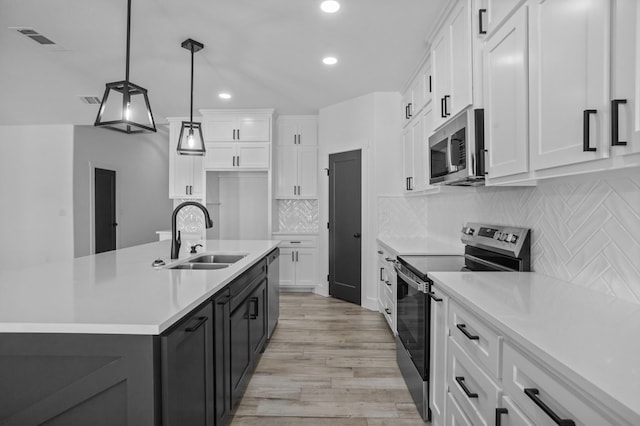 kitchen featuring stainless steel appliances, a kitchen island with sink, white cabinets, and decorative light fixtures