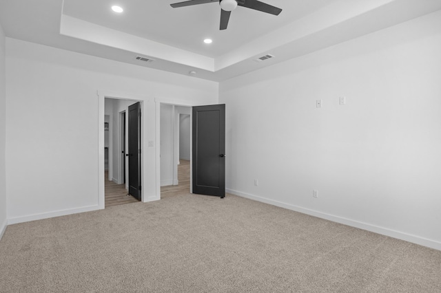 unfurnished bedroom with a raised ceiling, light carpet, and ceiling fan