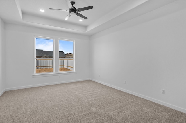 carpeted spare room featuring a raised ceiling and ceiling fan