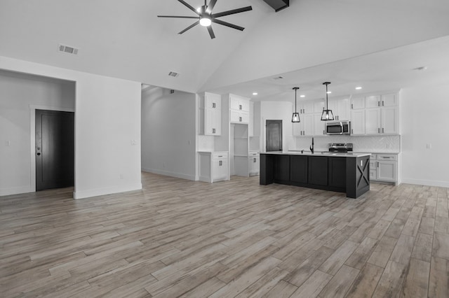 kitchen with appliances with stainless steel finishes, pendant lighting, white cabinets, a center island with sink, and light wood-type flooring