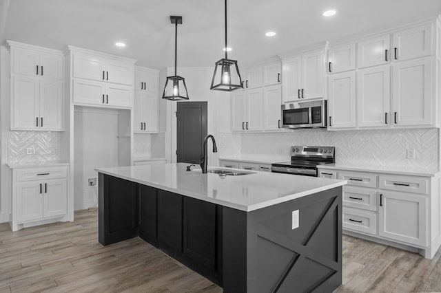 kitchen featuring appliances with stainless steel finishes, decorative light fixtures, sink, white cabinets, and a kitchen island with sink