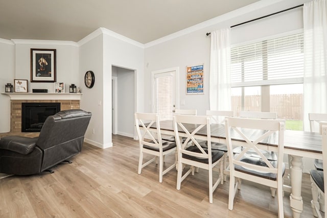 dining area featuring light wood finished floors, a fireplace, baseboards, and ornamental molding