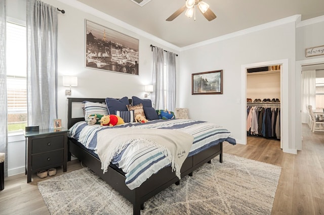 bedroom with a walk in closet, baseboards, light wood finished floors, and ornamental molding