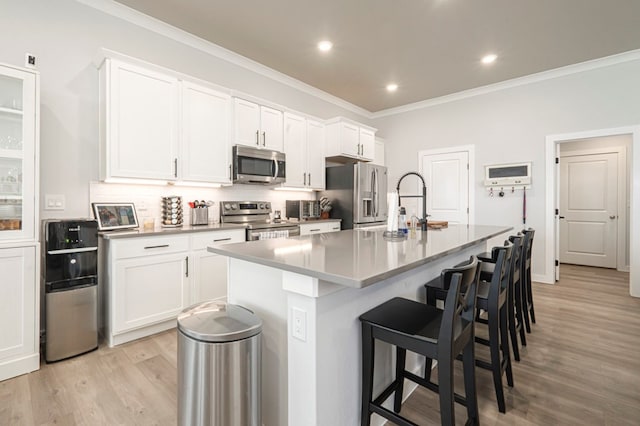 kitchen featuring a kitchen bar, a kitchen island with sink, ornamental molding, backsplash, and appliances with stainless steel finishes