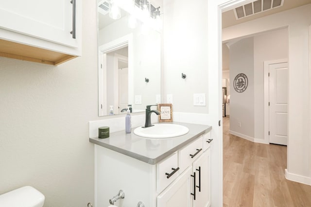 half bath with visible vents, toilet, wood finished floors, baseboards, and vanity