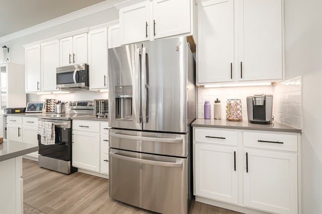 kitchen featuring ornamental molding, stainless steel appliances, light wood-style floors, white cabinetry, and tasteful backsplash