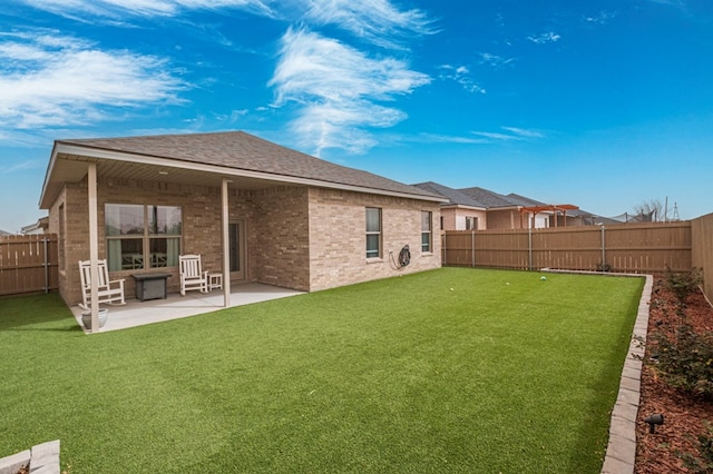 rear view of property featuring a yard, brick siding, a fenced backyard, and a patio area