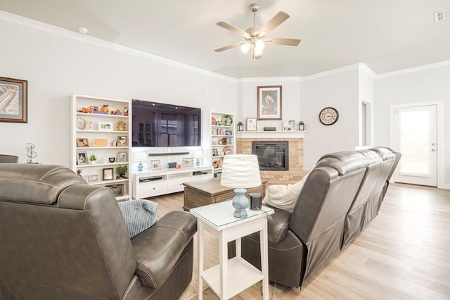 living room featuring light wood finished floors, visible vents, ornamental molding, a glass covered fireplace, and a ceiling fan