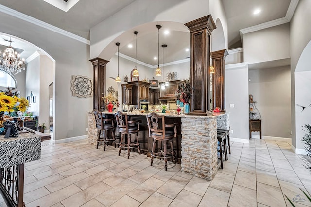 kitchen with a breakfast bar, ornamental molding, arched walkways, light stone countertops, and dark brown cabinets