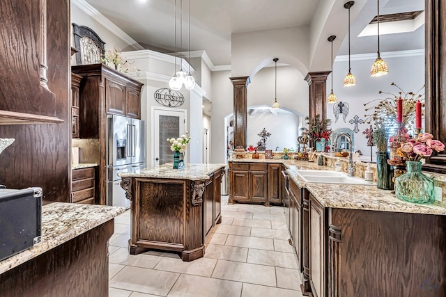 kitchen with light stone countertops, dark brown cabinetry, ornamental molding, high end fridge, and a sink