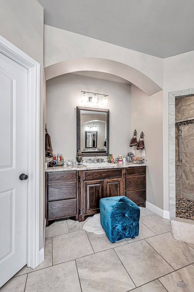 full bath featuring tile patterned flooring, tiled shower, vanity, and baseboards