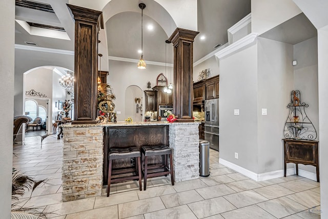 kitchen with a high ceiling, arched walkways, stainless steel appliances, dark brown cabinets, and a kitchen bar