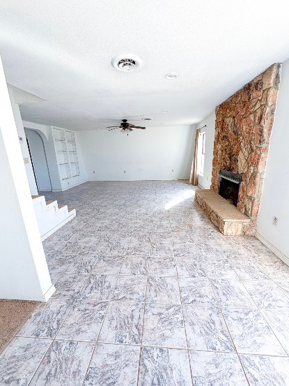 unfurnished living room featuring visible vents, a ceiling fan, stairway, a textured ceiling, and a fireplace