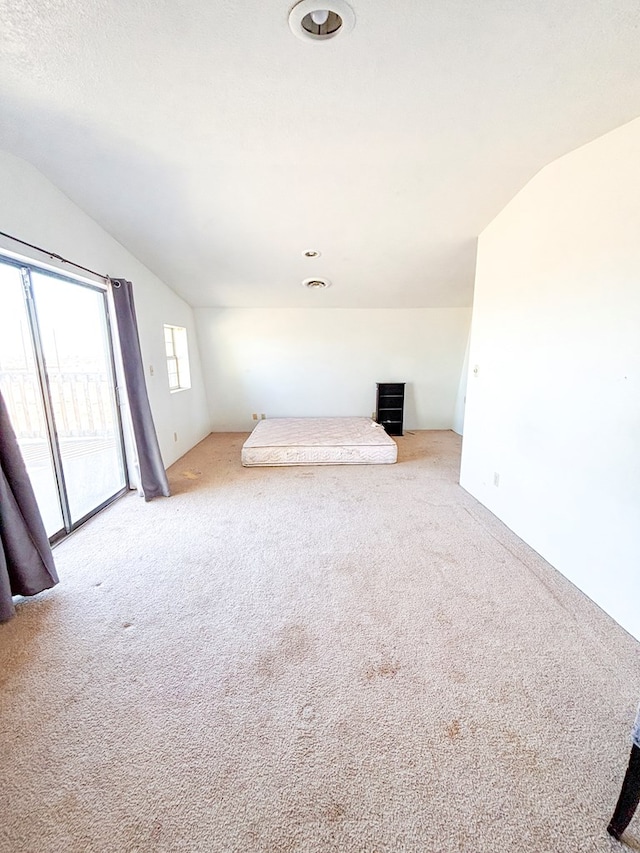 unfurnished bedroom featuring vaulted ceiling, access to outside, carpet, and visible vents