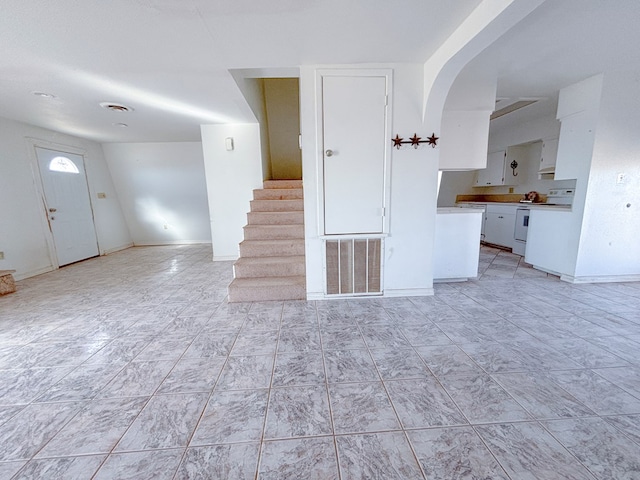 unfurnished living room featuring baseboards, stairs, visible vents, and arched walkways