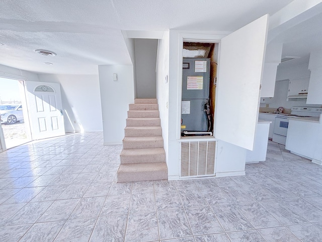 stairway featuring a textured ceiling, baseboards, visible vents, and heating unit