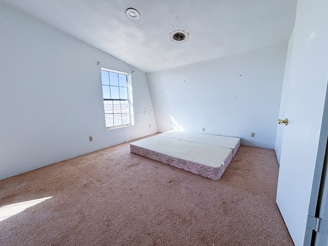 unfurnished bedroom with carpet, vaulted ceiling, and a textured ceiling