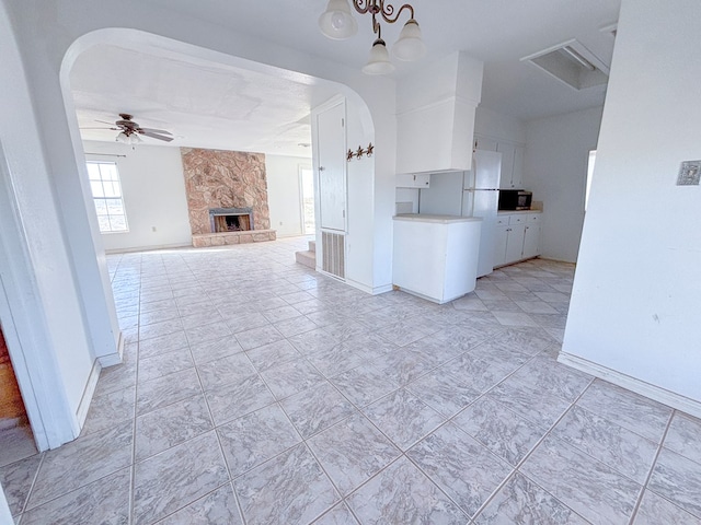 kitchen featuring arched walkways, white cabinets, a ceiling fan, and a stone fireplace