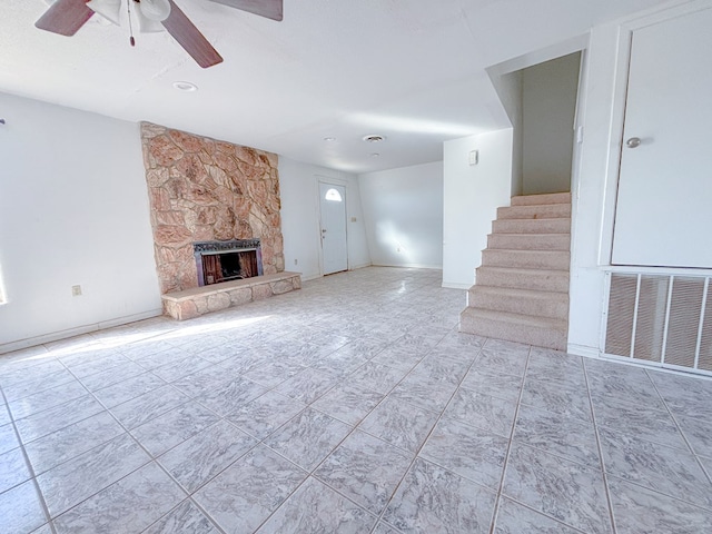 unfurnished living room featuring visible vents, stairway, ceiling fan, a stone fireplace, and baseboards