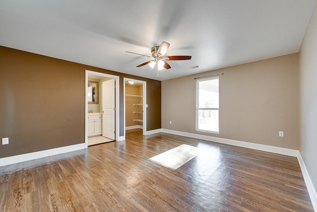 unfurnished bedroom featuring a spacious closet, a closet, ceiling fan, and hardwood / wood-style flooring