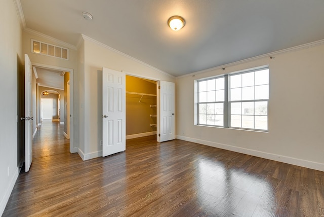 unfurnished bedroom with a spacious closet, dark hardwood / wood-style floors, crown molding, lofted ceiling, and a closet