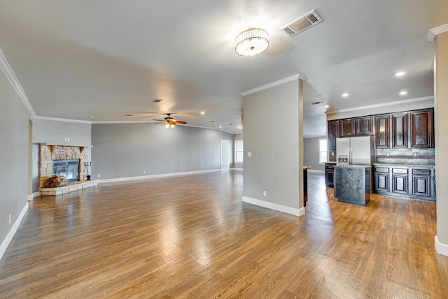 unfurnished living room with a fireplace, wood-type flooring, ceiling fan, and crown molding