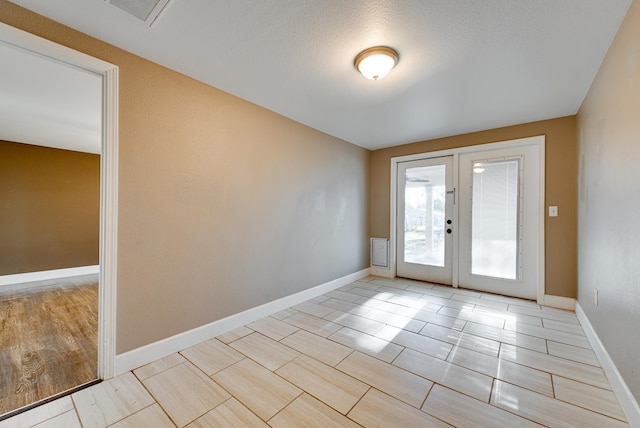 doorway with french doors, light wood-type flooring, and a textured ceiling