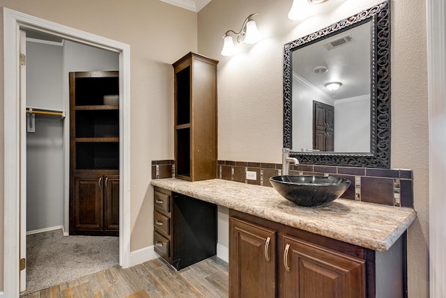 bathroom with vanity, wood-type flooring, ornamental molding, and tasteful backsplash