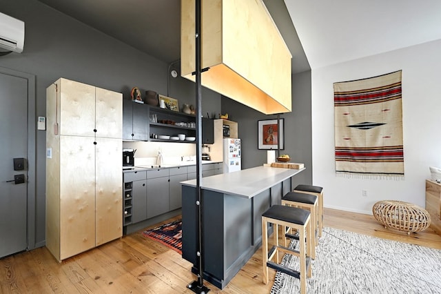 kitchen with freestanding refrigerator, a peninsula, an AC wall unit, light wood-type flooring, and open shelves