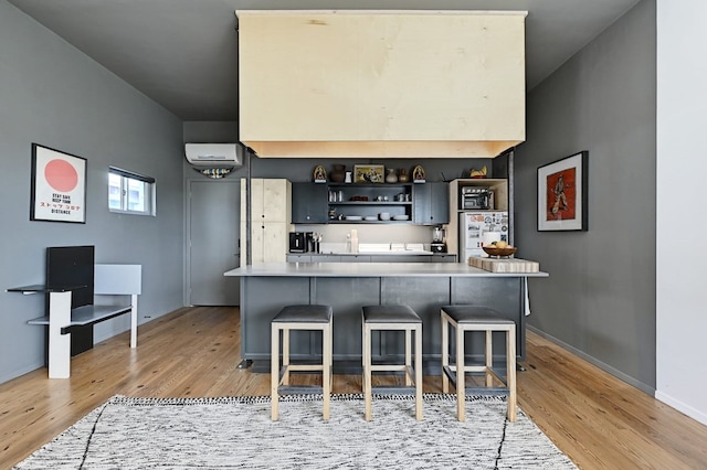 kitchen featuring light wood finished floors, a kitchen breakfast bar, light countertops, an AC wall unit, and open shelves