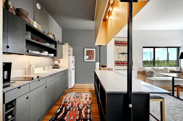 kitchen with black electric stovetop, a sink, light countertops, open shelves, and light wood finished floors